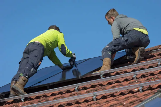 Wierden, Overijssel, Netherlands, march 24th 2020, low angle close-up of two male workers standing on top of a residential building with orange roof tiles, mounting solar panels on a frame over the rooftiles - this form of renewable energy for house owners is gaining popularity, the total solar panel power production in the Netherlands in 2020 increased by more than 50% compared to 2019